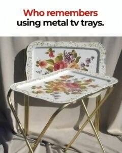 Two vintage metal tv trays with floral designs, one folded, against a neutral background